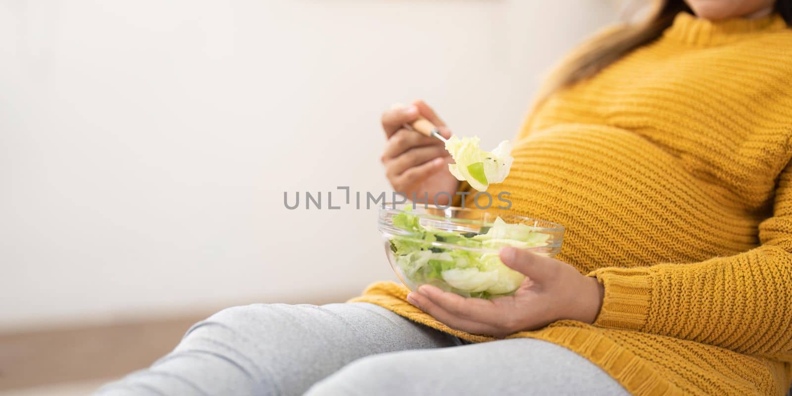 Happy pregnant young woman sitting and eating salad at home.