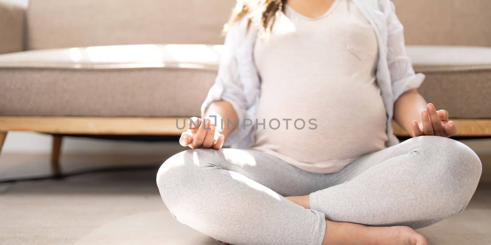 Relaxed Asian pregnant woman meditating in her living room, lotus pose, concentrating breath.
