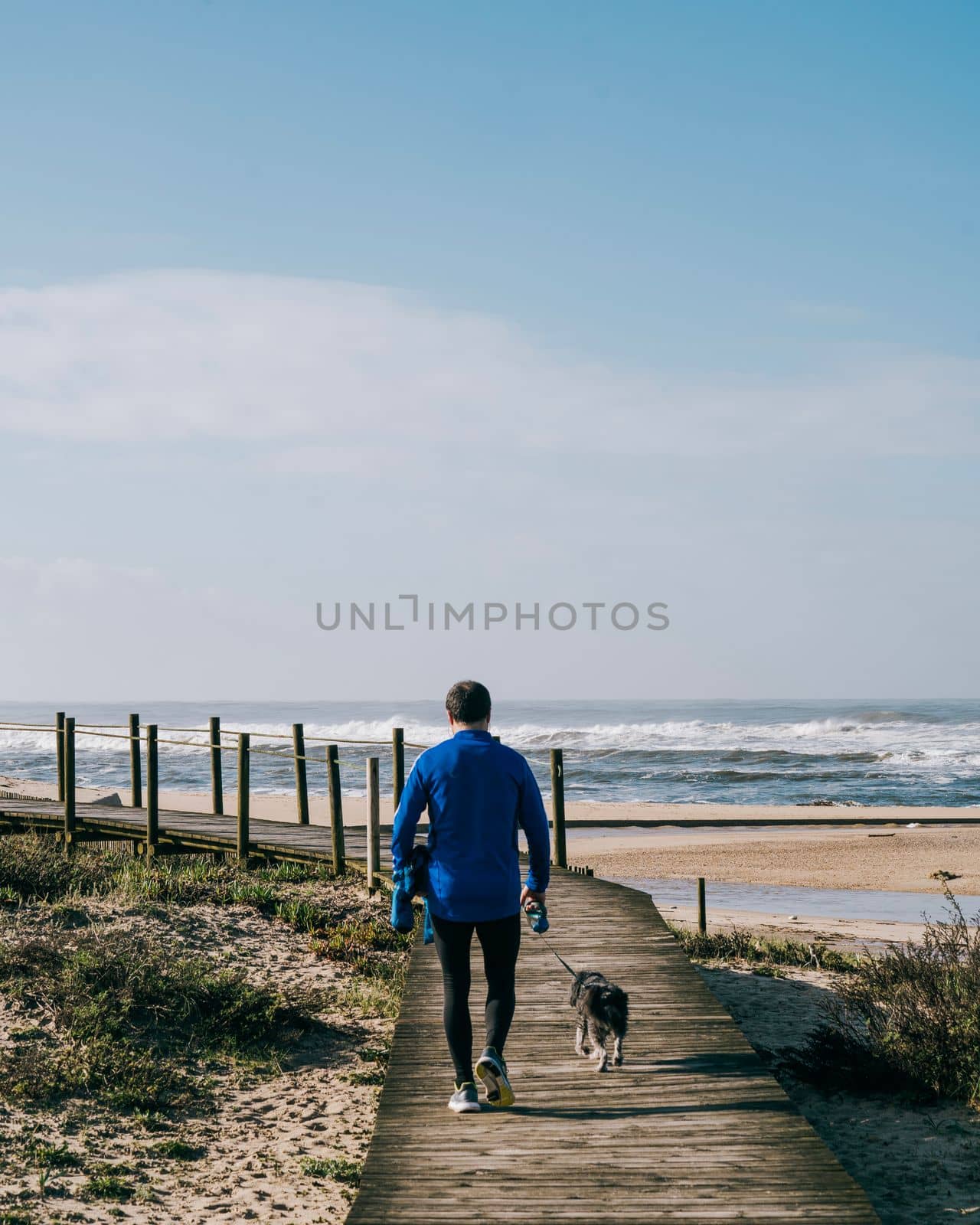 Sports man walking with his dog over a wooden path against blue sky and sea waves