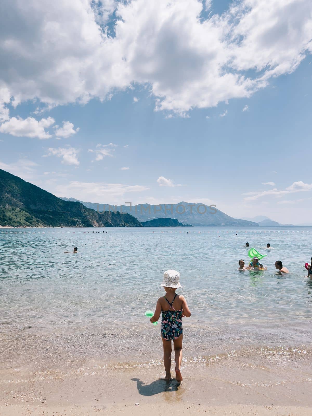 Little girl walks along the sand towards the sea. Back view by Nadtochiy