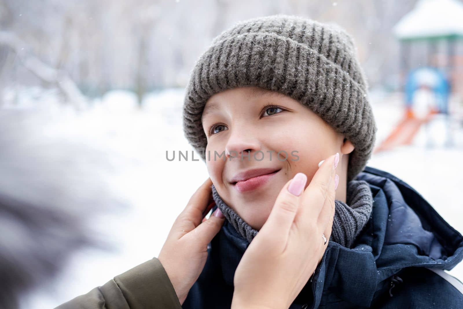 Smiling boy in winter clothing outdoor and mother hands applying cream to his face to protect skin from wind and cold