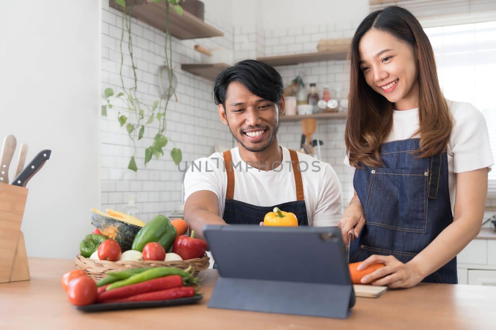 Romantic couple is cooking on kitchen. Handsome man and attractive young woman are having fun together while making salad. Healthy lifestyle concept. by wichayada