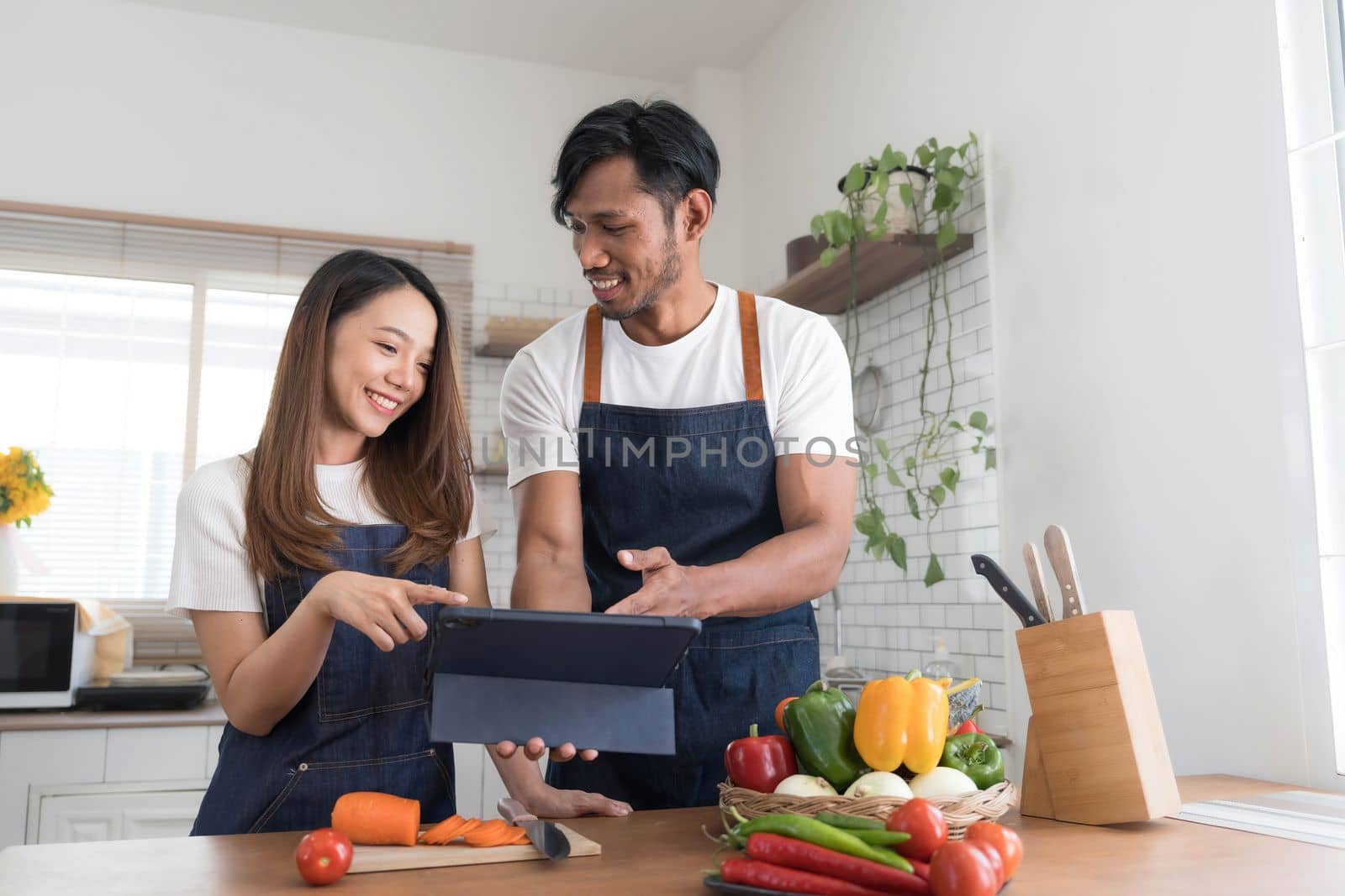 Romantic couple is cooking on kitchen. Handsome man and attractive young woman are having fun together while making salad. Healthy lifestyle concept. by wichayada