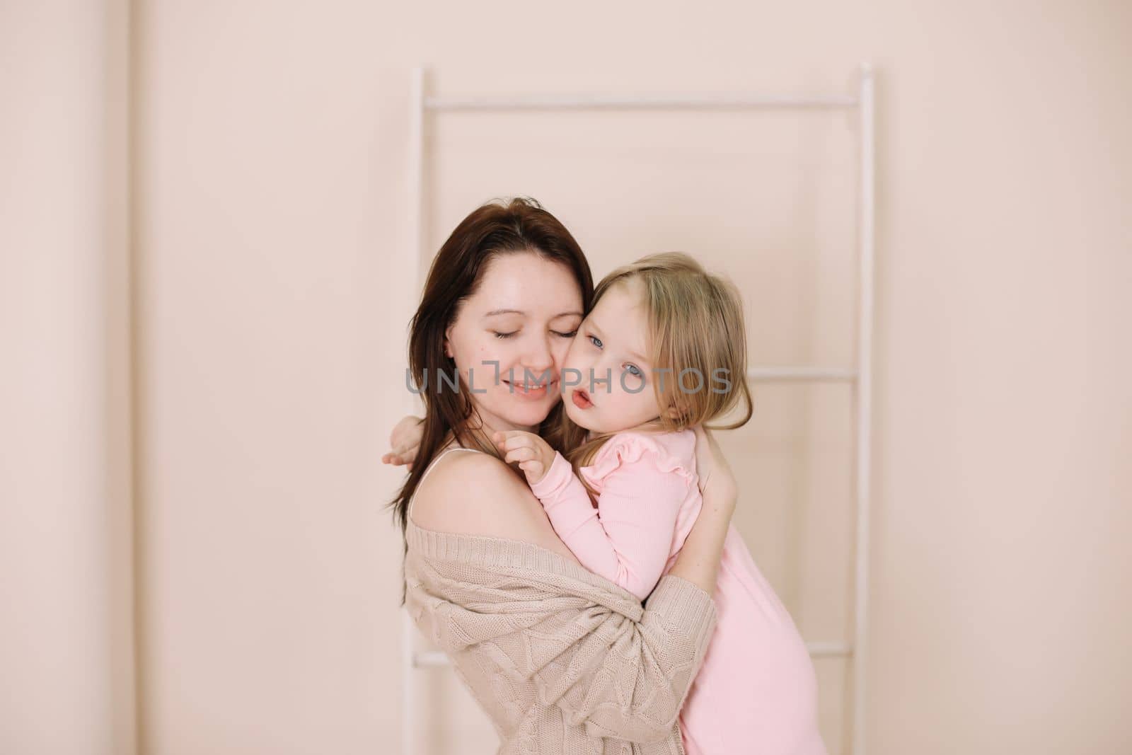 Woman in light clothes have fun with cute child baby girl 3 years old. Mommy little kid daughter on beige background studio portrait. Mother's Day love family parenthood childhood concept by paralisart