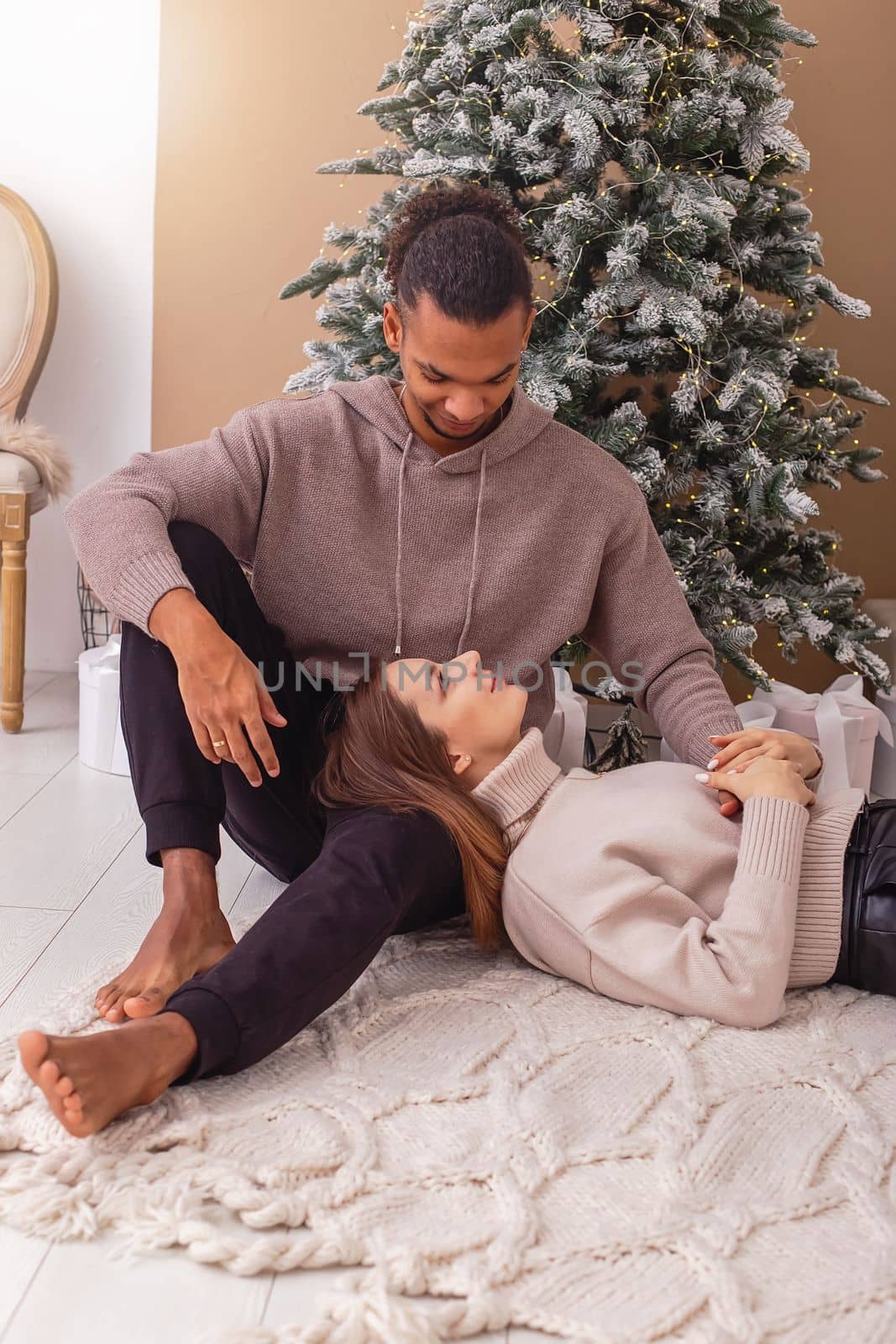 A happy girl, lies on the lap of a stylish guy near the Christmas tree in the room by Zakharova