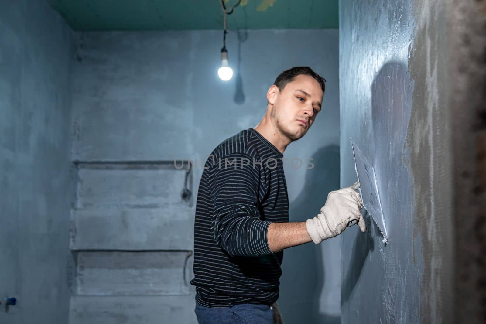 man applies insulation to a bathroom wall with trowel by Edophoto