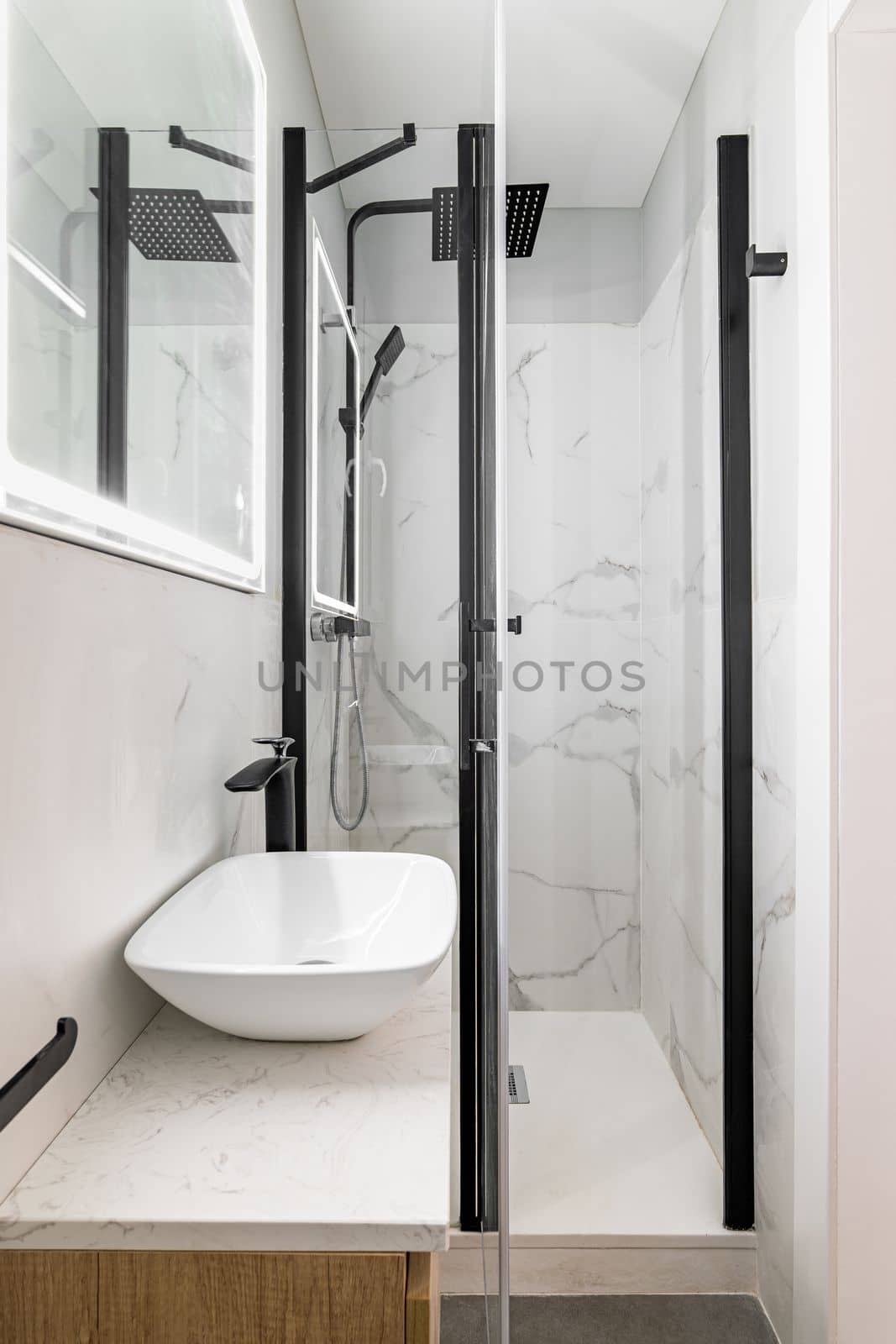 Bathroom with modern designer renovation and fittings. Vanity sink with black faucet. Walls of white granite tiles and square mirror with built-in light. by apavlin