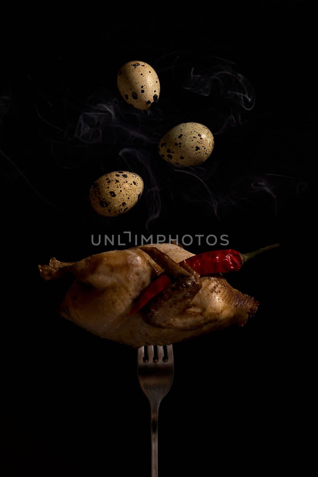 Quail fork eggs. Fried quail on a fork close-up on a black background serhu three quail eggs fly under the wing of a red hot pepper pod. vertical photo. by Matiunina