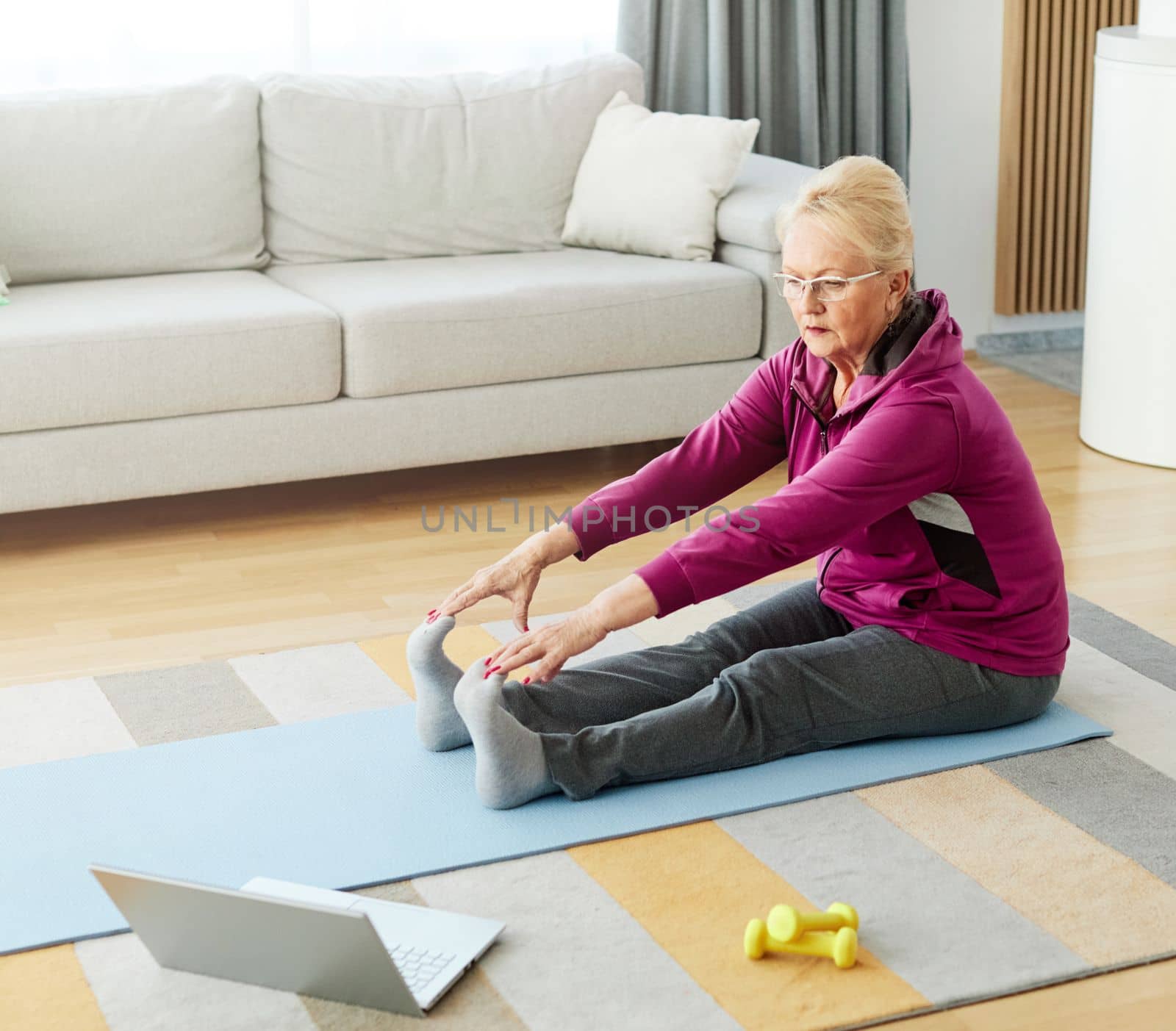 Senior woman exercise stretching yoga using laptop online instructions at home health care