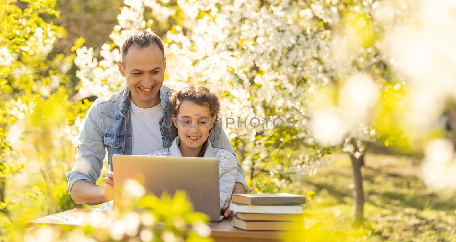 Caring young father helps little daughter, studying together watch online lesson on laptop, attentive dad and small girl child learning at home, have web class on computer on quarantine. outdoor.