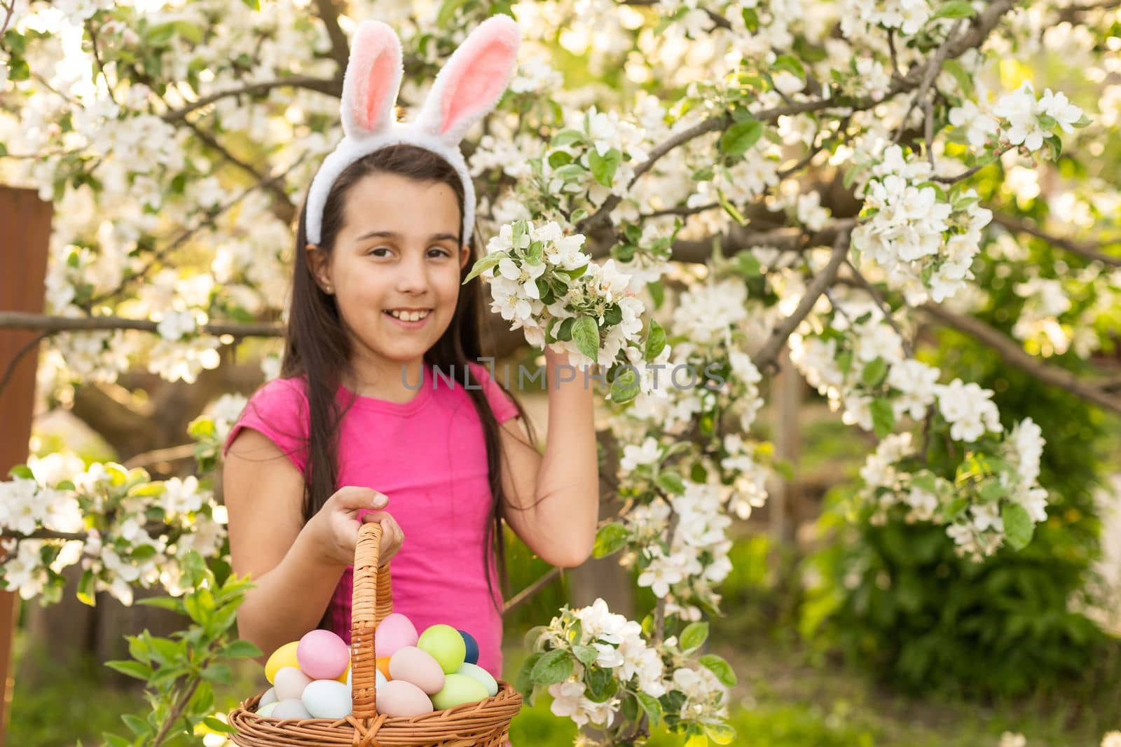 A little girl with pink rabbit ears. painted eggs in the park. Easter. Copy space. by Andelov13