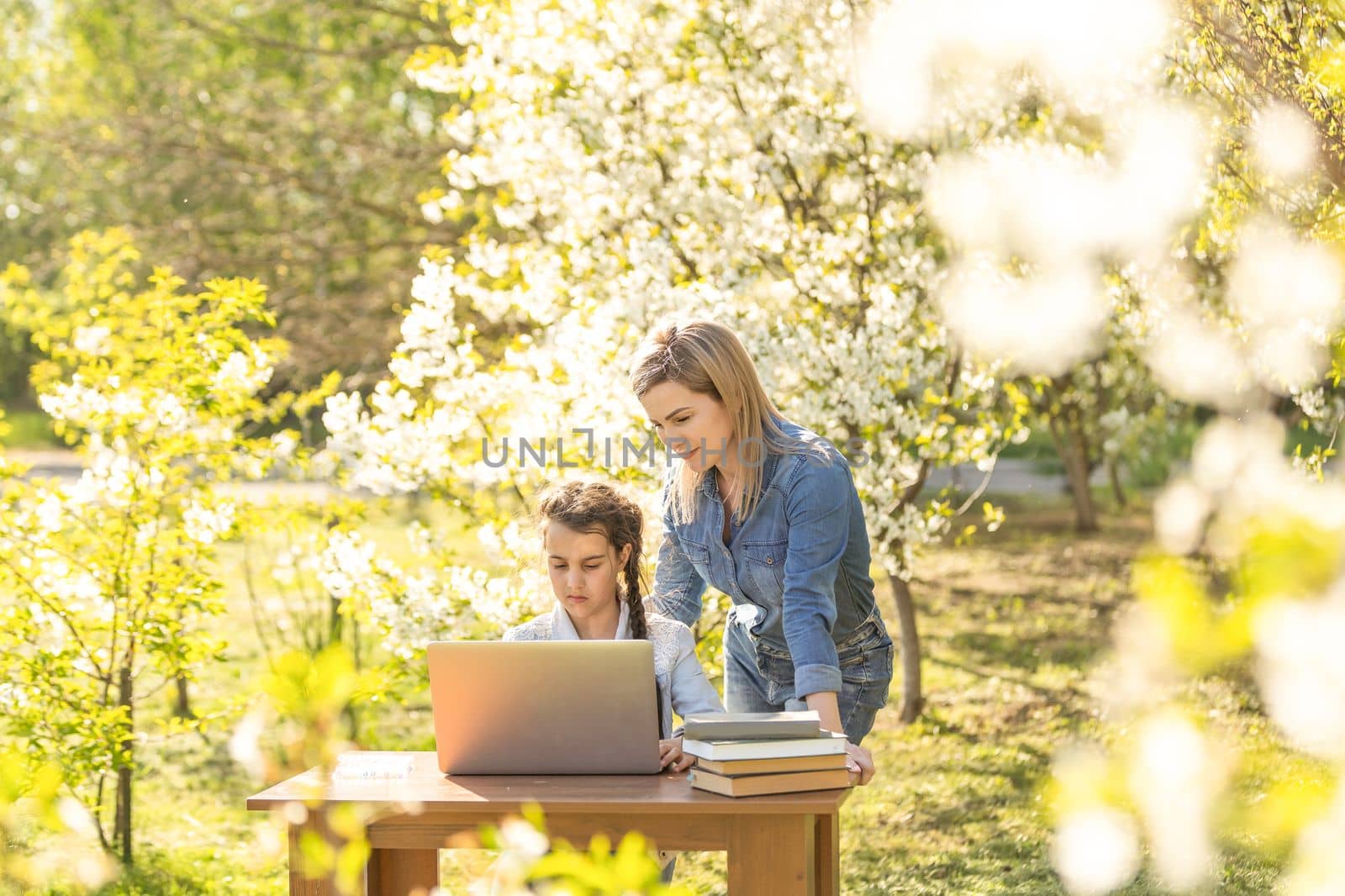 Woman and little girl laying on the spring flower field outdoors - having fun using a laptop. by Andelov13