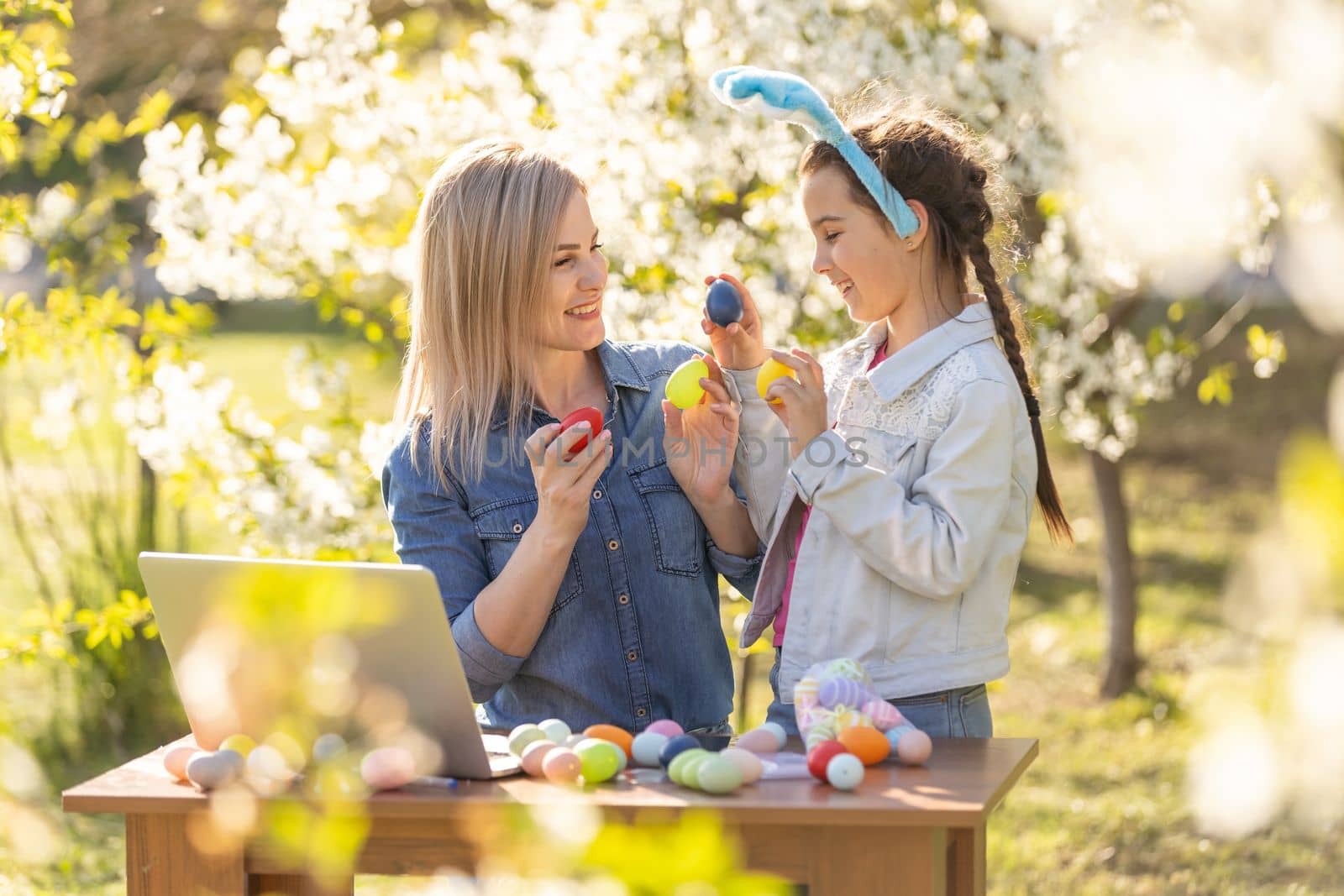 mother and daughter paint easter eggs with laptop.