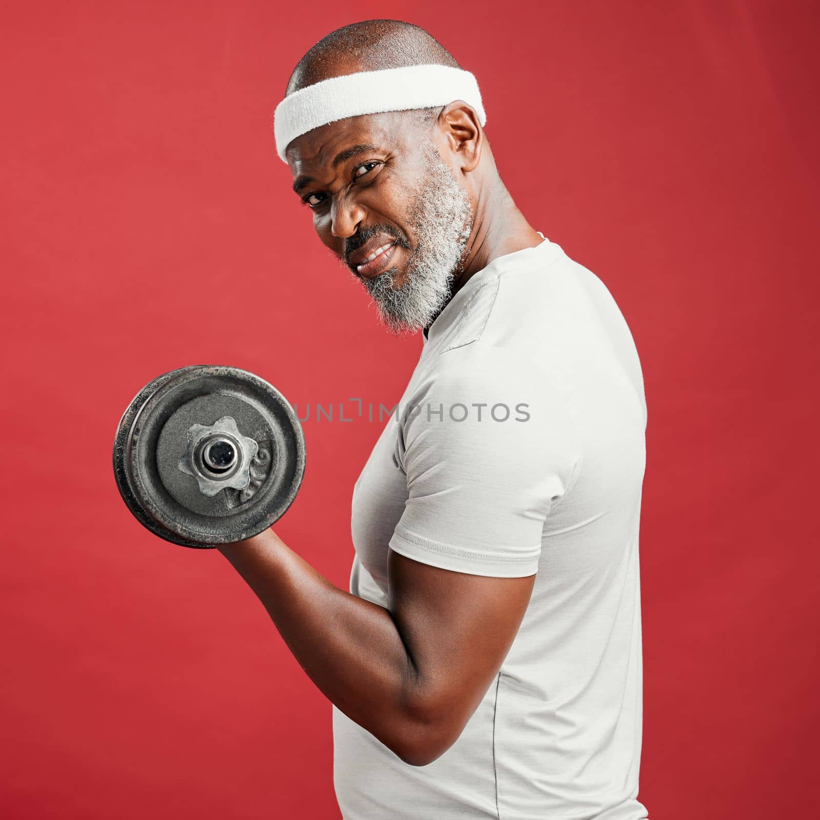 Confident mature african american man standing alone against a red background in a studio and posing with dumbbells. Focused black man feeling sporty and fit while working out. A heathy lifestyle by YuriArcurs