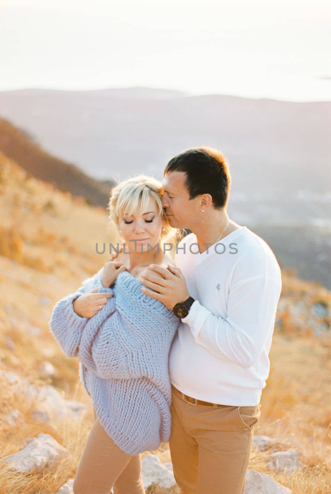 Man hugs woman by the shoulders while standing on a mountain by Nadtochiy