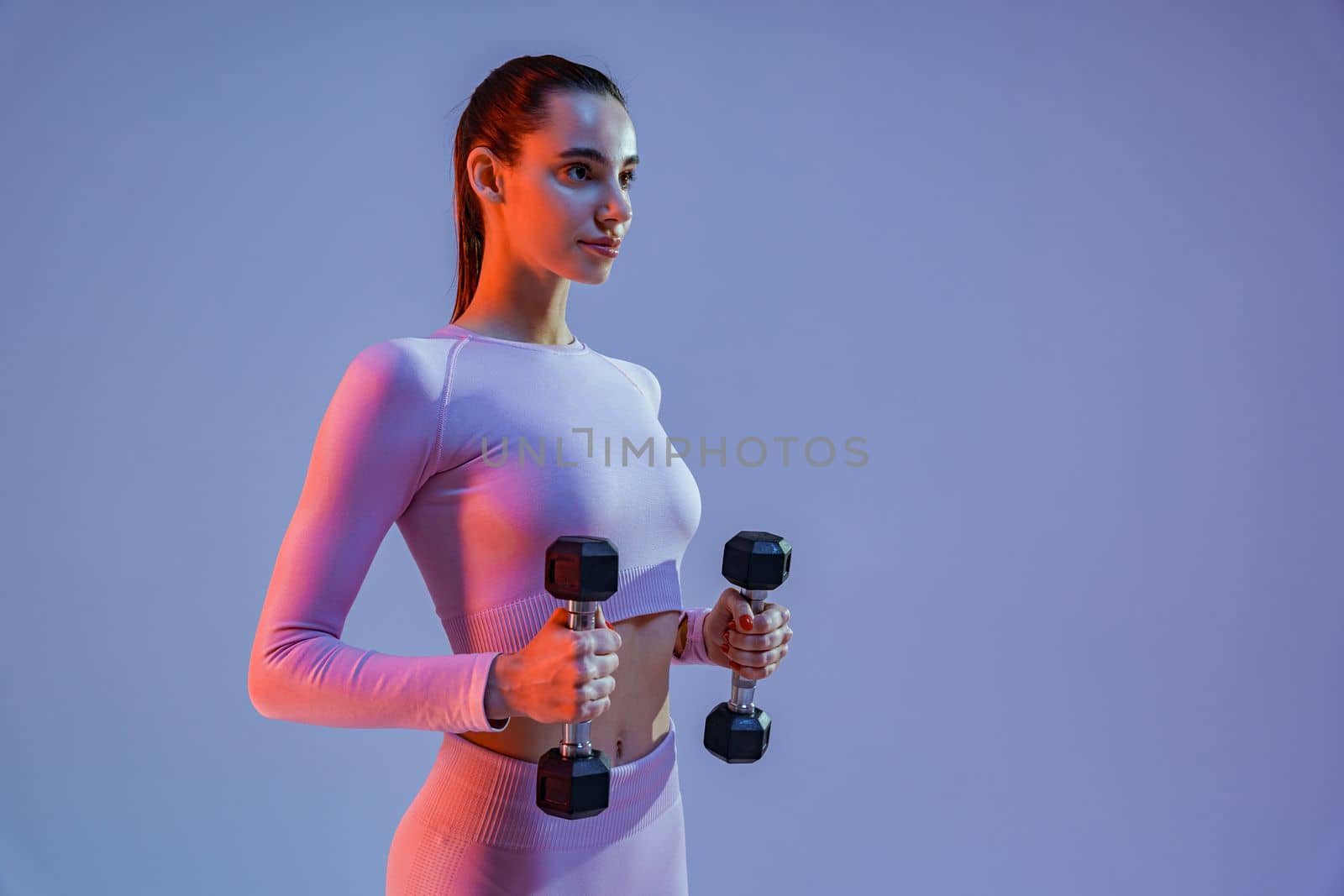 Fitness woman doing exercises with dumbbells on studio background and looking at side by Yaroslav_astakhov