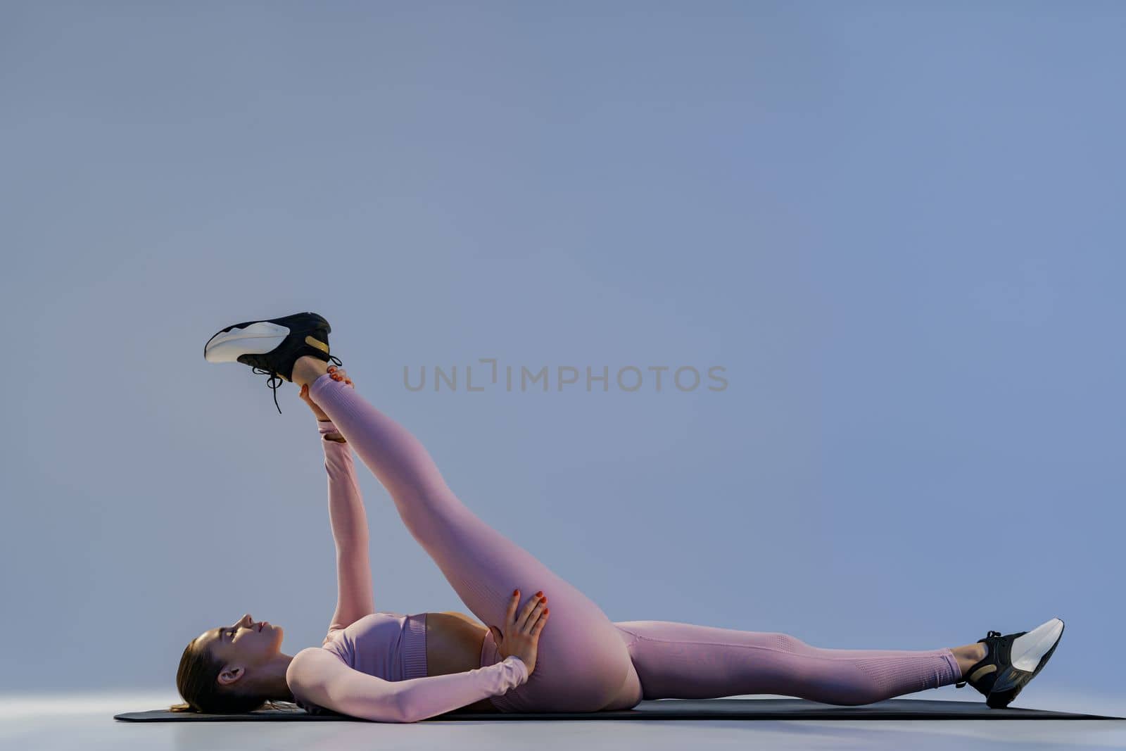Athletic woman in sportswear doing stretching exercises on yoga mat on studio background