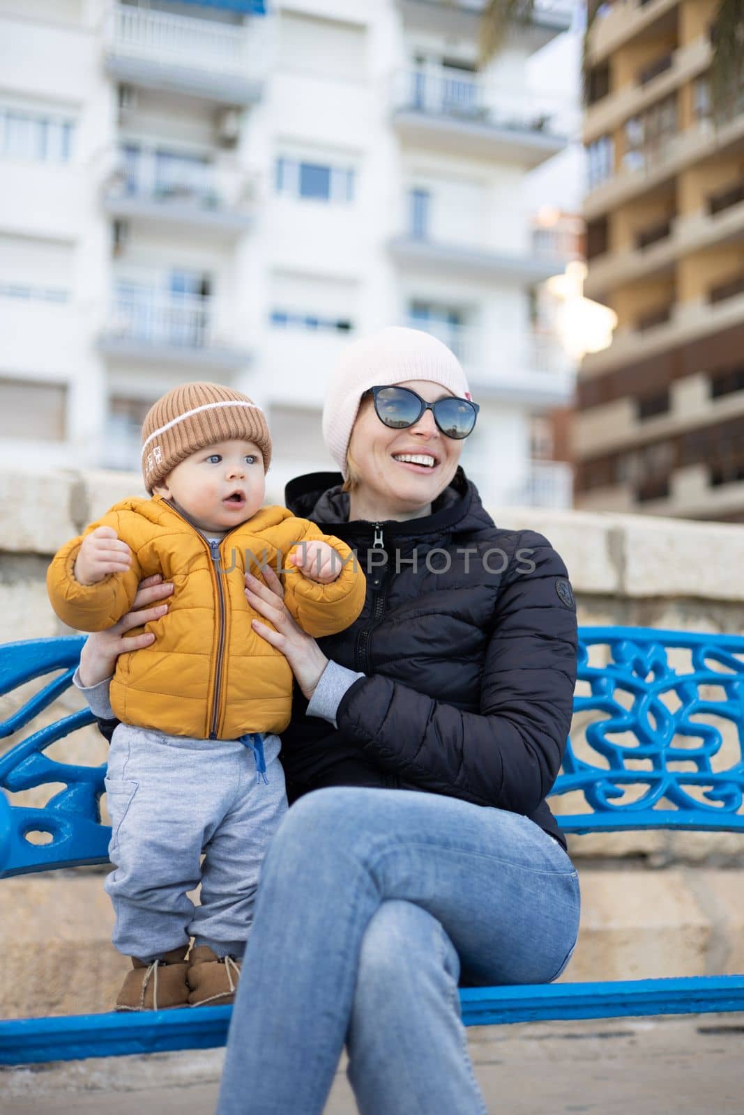 Young mother with her cute infant baby boy child on bench in city park. by kasto