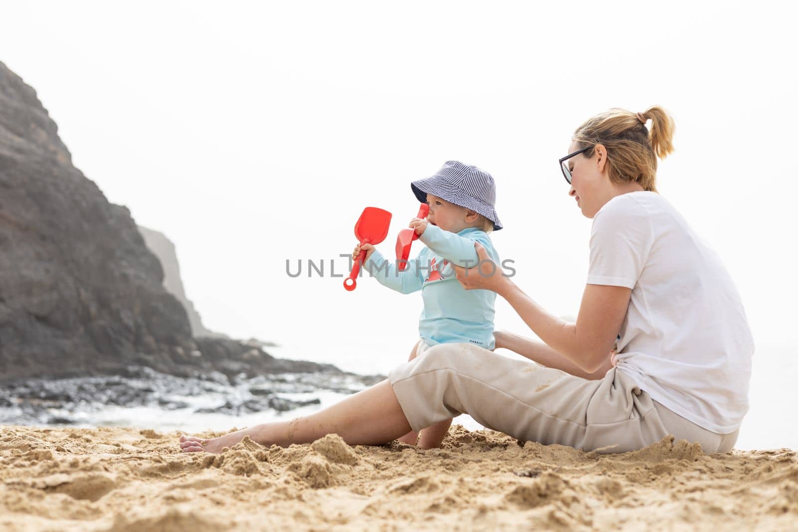 Mother playing his infant baby boy son on sandy beach enjoying summer vacationson on Lanzarote island, Spain. Family travel and vacations concept. by kasto