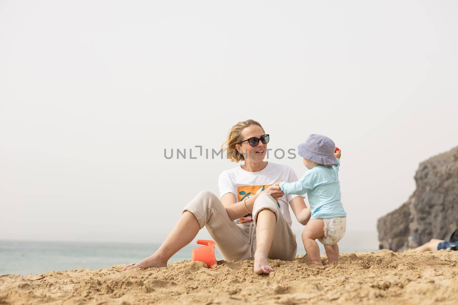 Mother playing his infant baby boy son on sandy beach enjoying summer vacationson on Lanzarote island, Spain. Family travel and vacations concept. by kasto