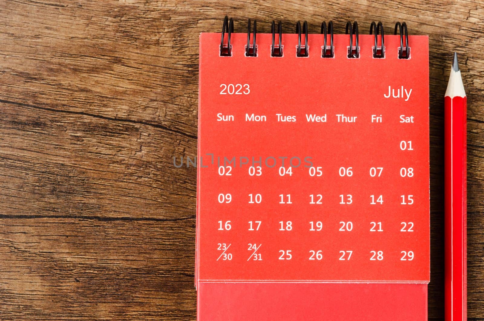 Red July 2023 Monthly desk calendar for 2023 year with pencil on wooden background.