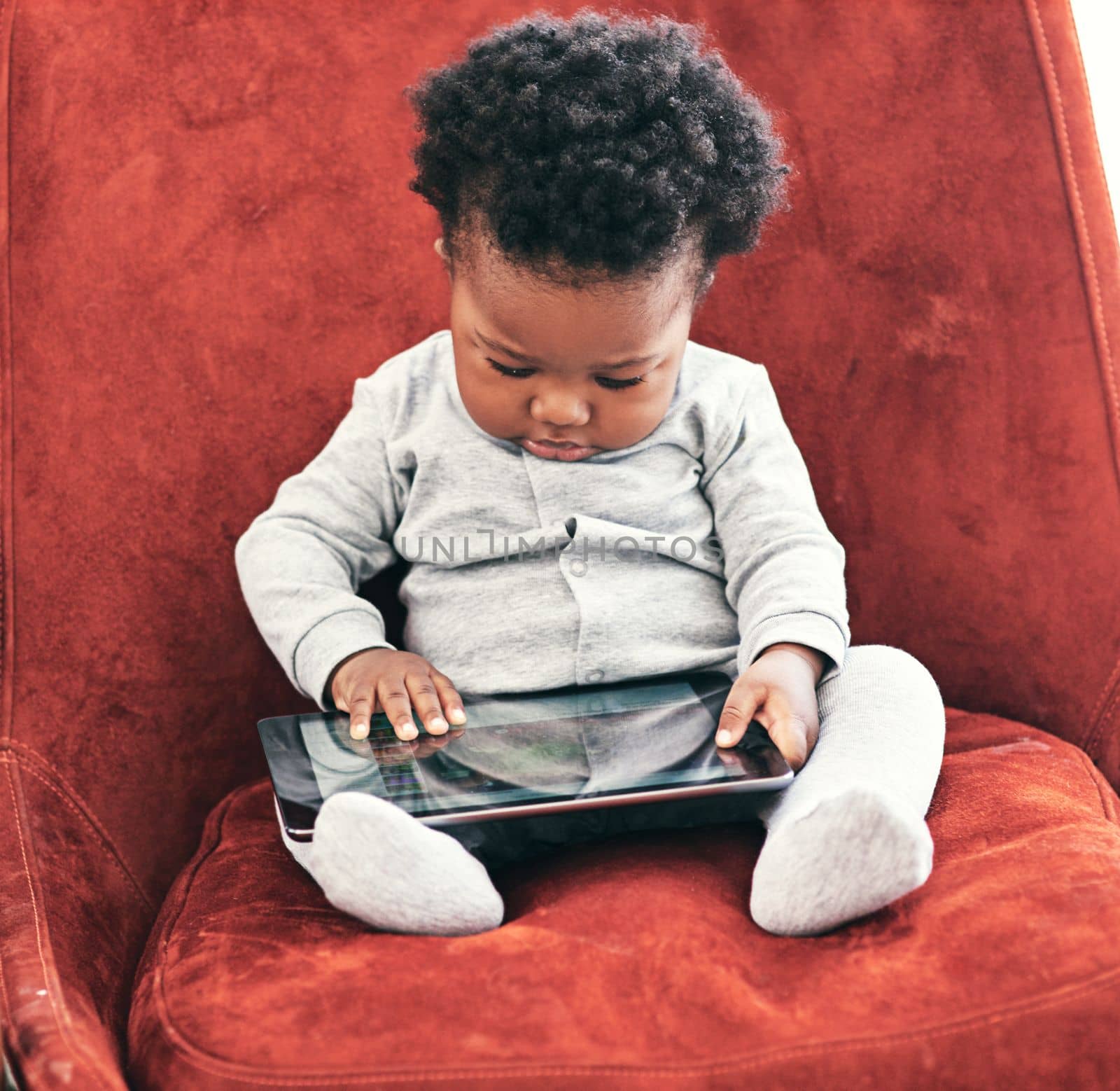 Hes a curious fella. a little baby boy sitting in a chair holding a digital tablet. by YuriArcurs