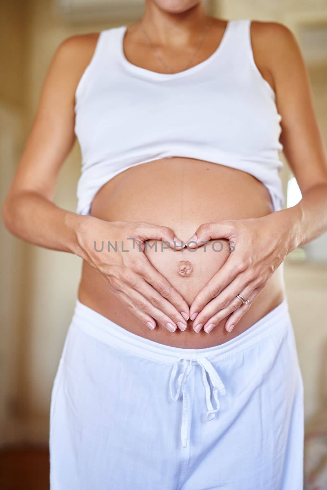Unconditional love. a pregnant woman holding her belly with her hands forming a heart shape. by YuriArcurs