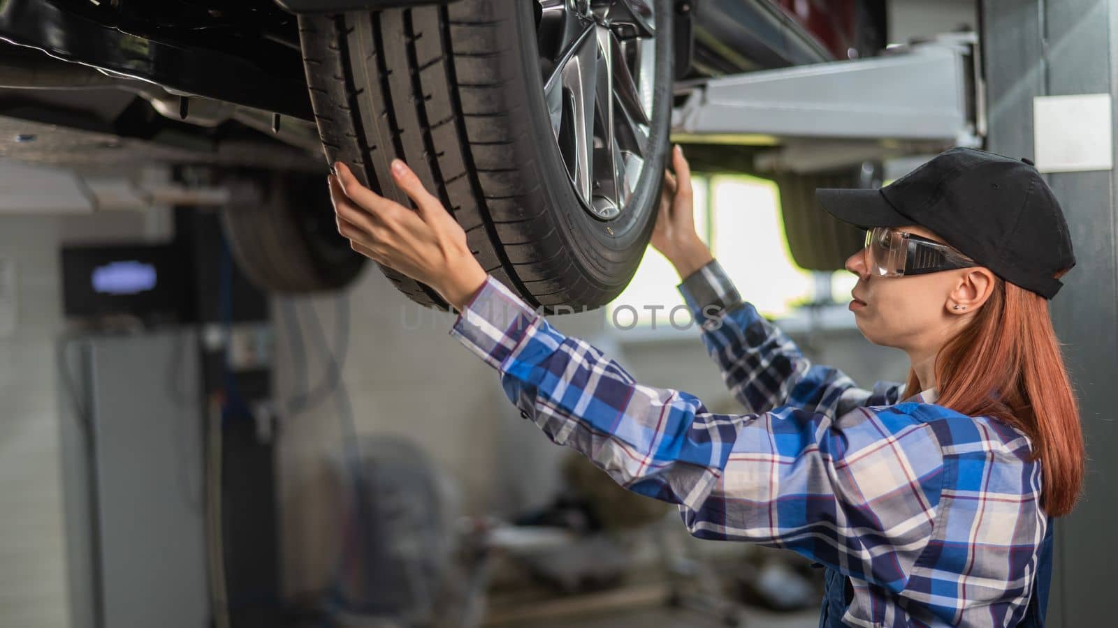 Female mechanic adjusting the tire of the car that is on the lift. A girl at a man's work. by mrwed54