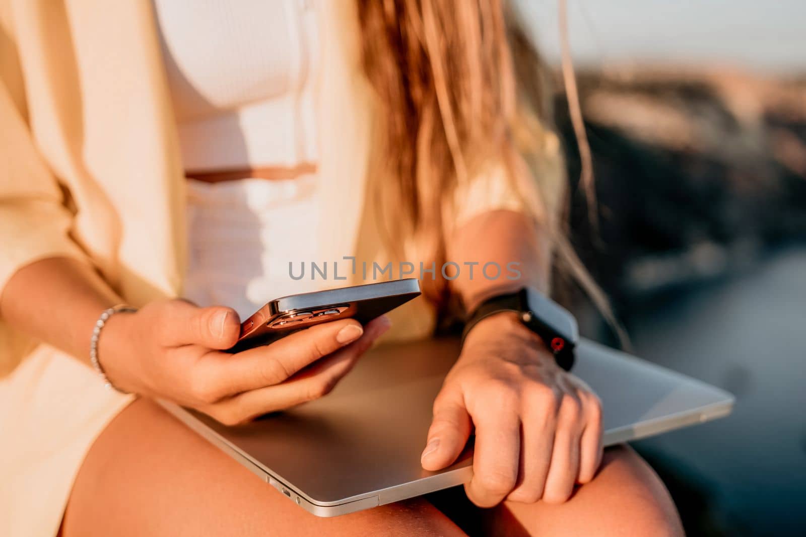 Successful business woman in yellow hat working on laptop by the sea. Pretty lady typing on computer at summer day outdoors. Freelance, travel and holidays concept.