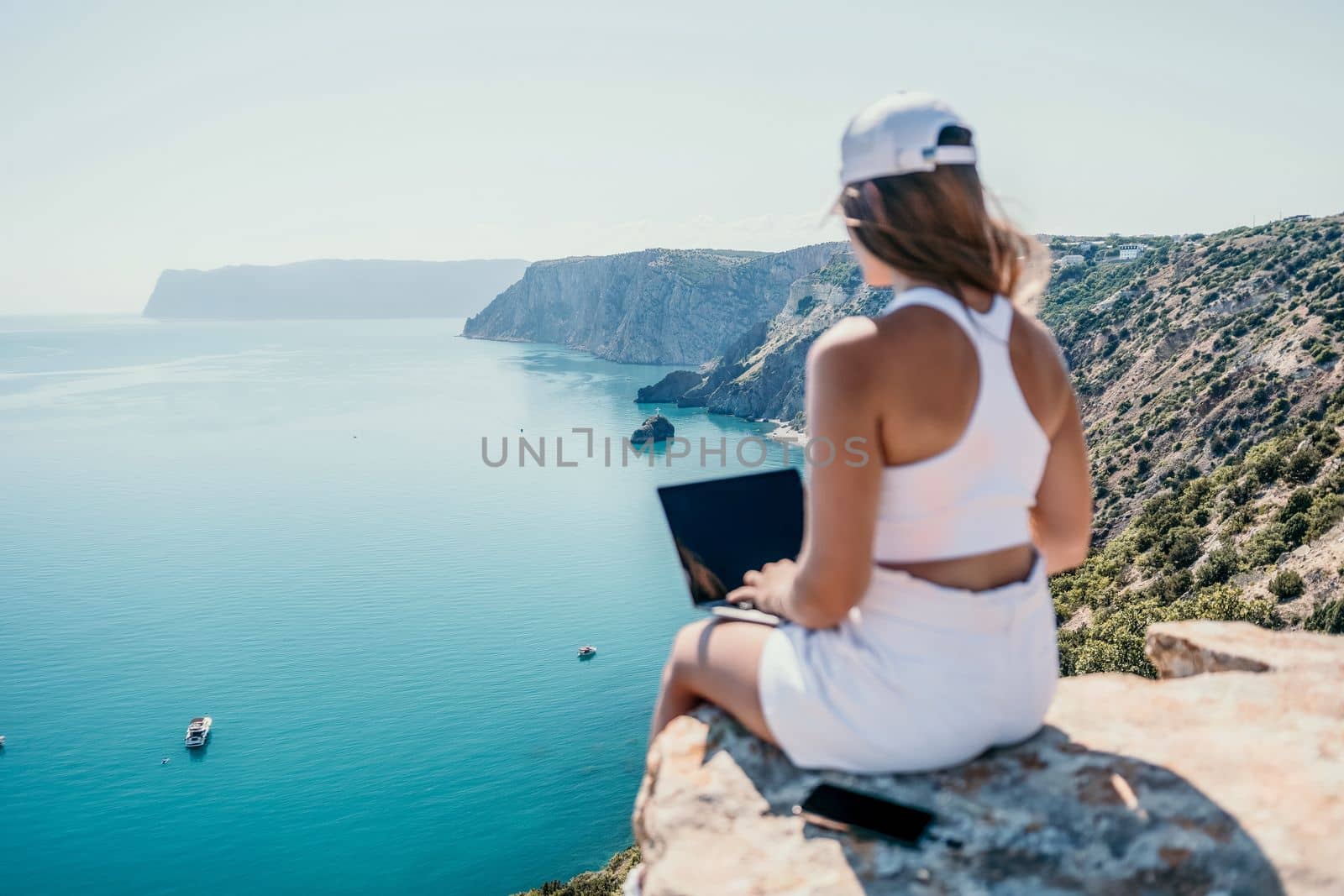 Digital nomad, Business woman working on laptop by the sea. Pretty lady typing on computer by the sea at sunset, makes a business transaction online from a distance. Freelance, remote work on vacation by panophotograph