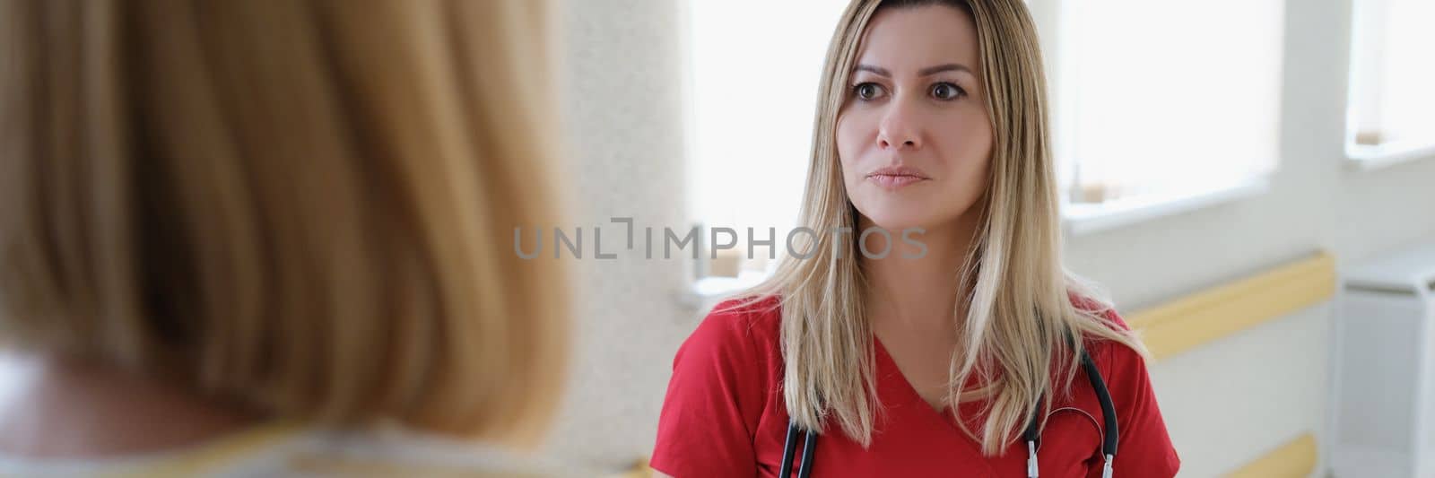 Female therapist doctor in red uniform consults and listens to patient in clinic by kuprevich