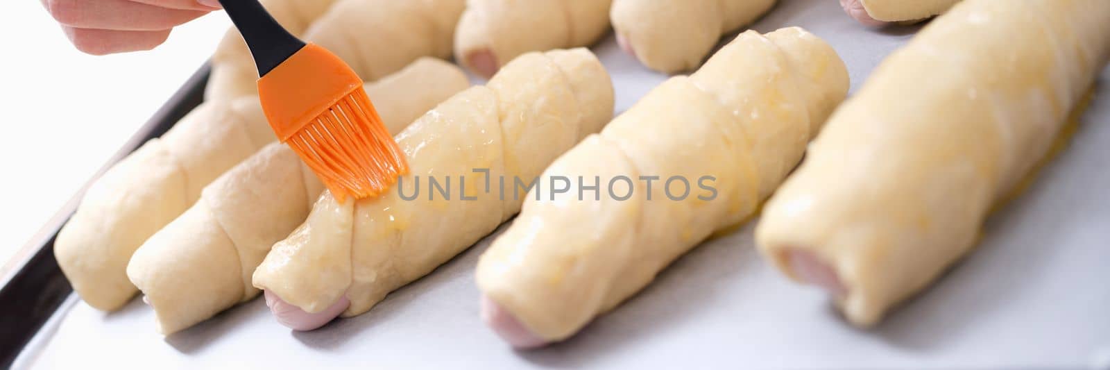 Female cook greases sheet of dough with melted butter and prepares sausage wrapped in dough. Delicious snack and cooking hot dog concept