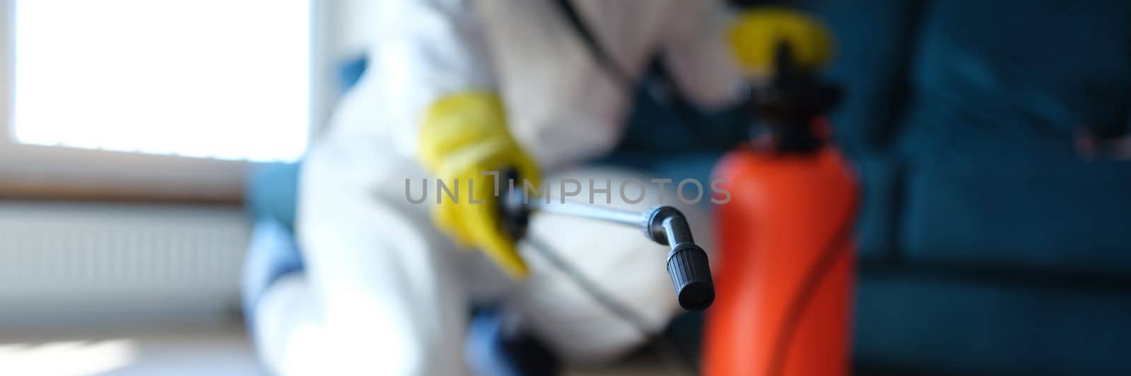 Person in white protective suit in hotel or apartment sprays disinfectant against viruses or rodents by kuprevich