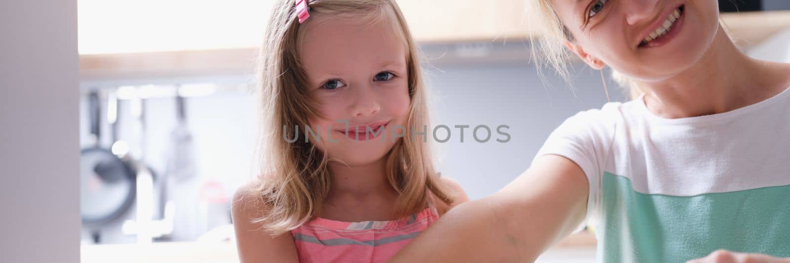 Happy young mother and little child daughter rolls out dough on kitchen table with pin by kuprevich