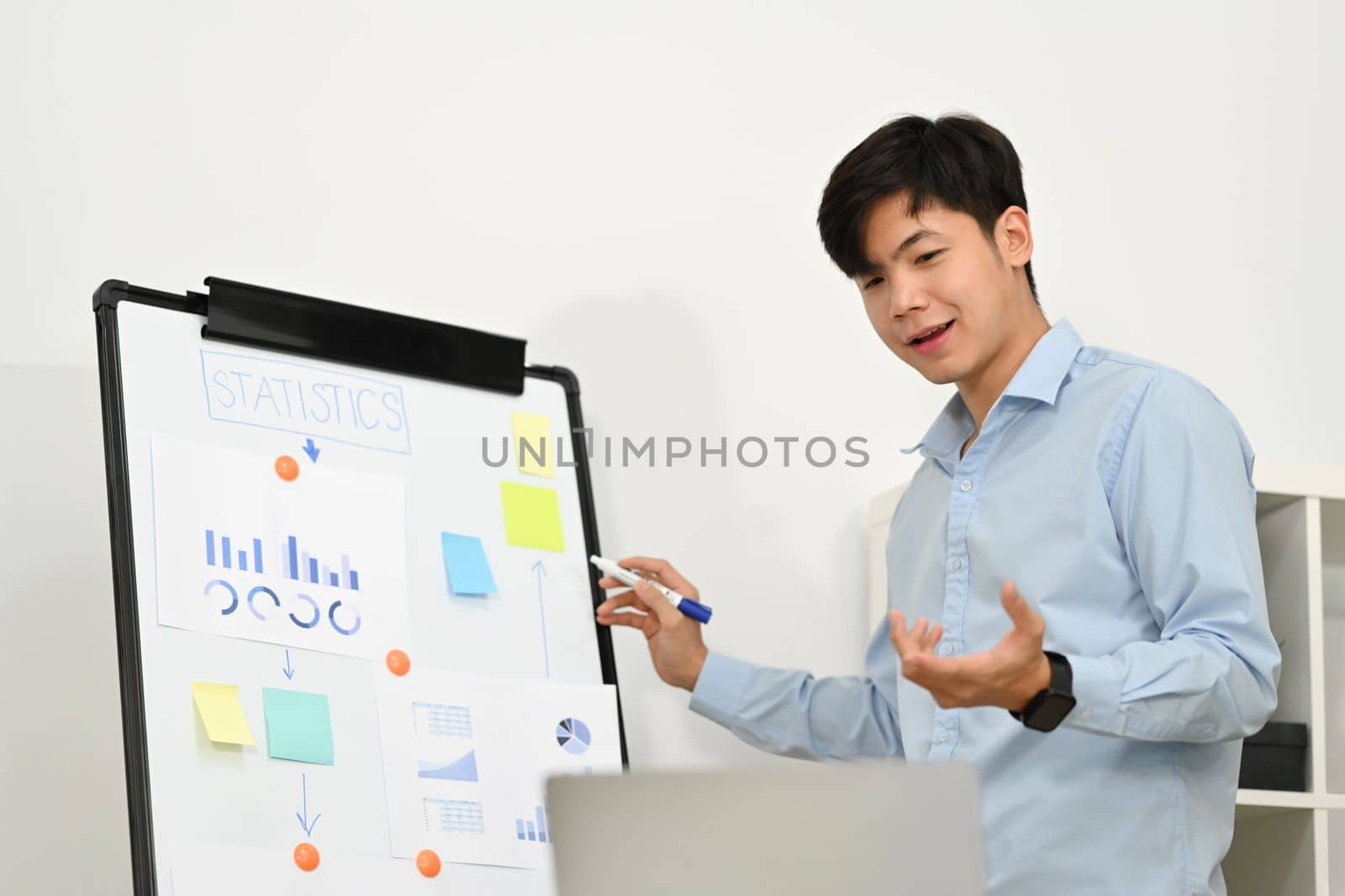 Smiling start up businessman explaining business data on whiteboard during online conference via laptop computer.