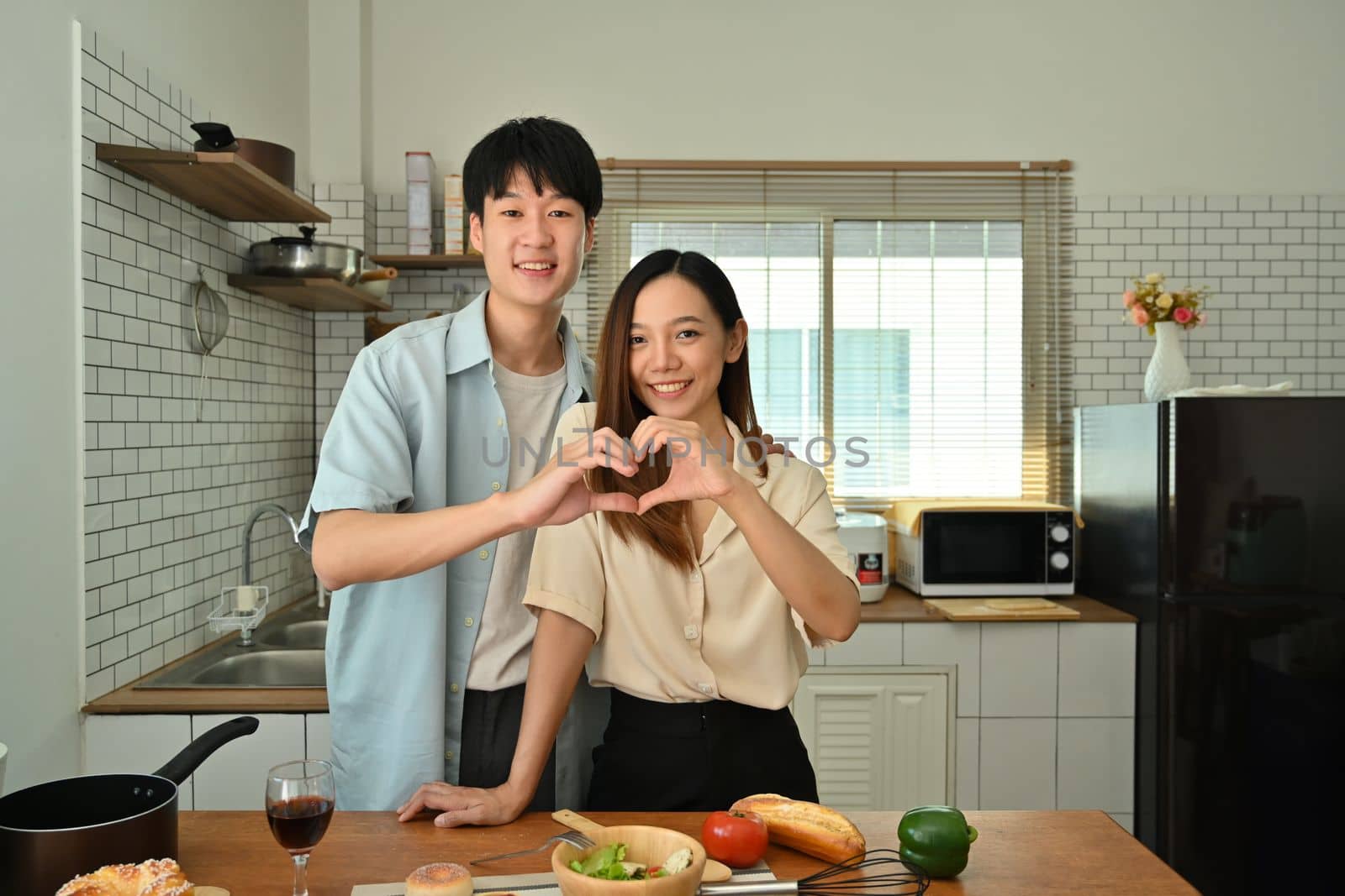 Beautiful young married couple making heart shape with their hands and smiling to camera. Love, relationship and family by prathanchorruangsak