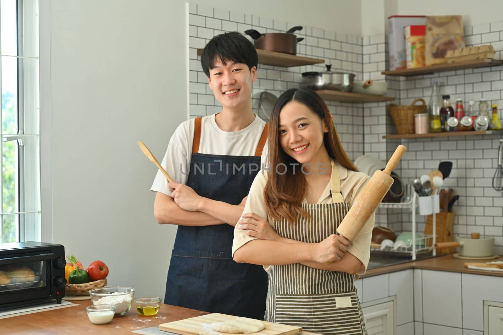 Happy married couple with rolling pins in their hand, preparing dinner in modern kitchen, enjoying leisure time at home.
