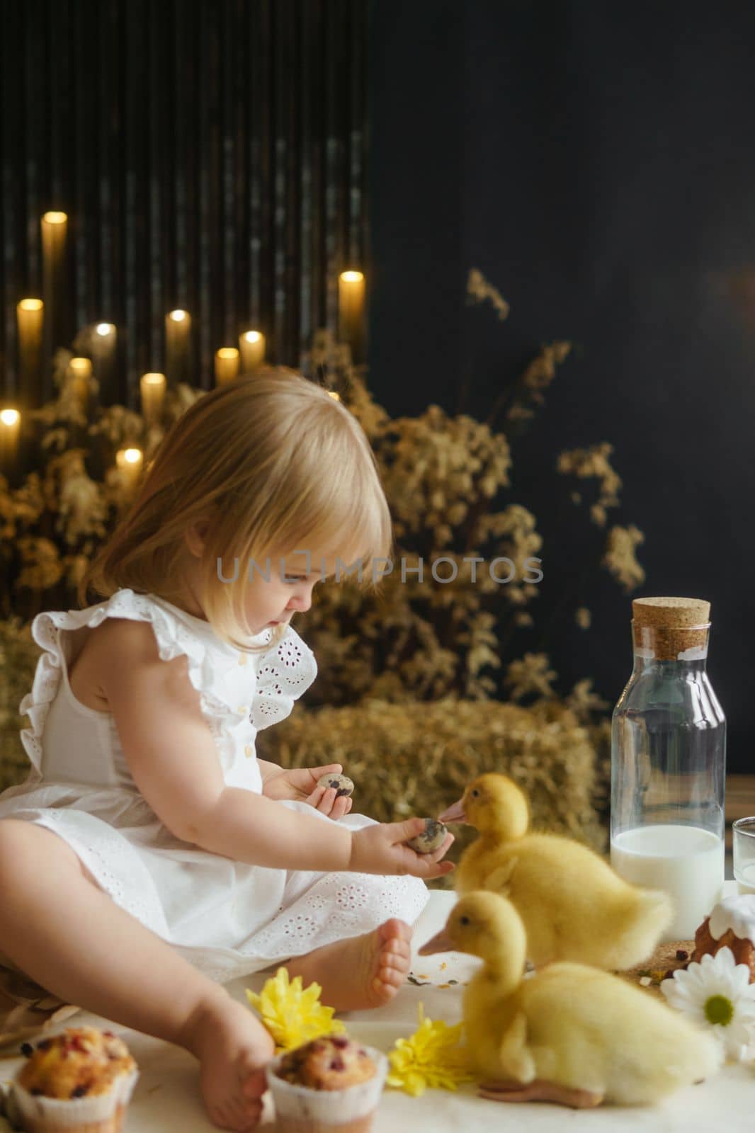 A little girl is sitting on the Easter table and playing with cute fluffy ducklings. The concept of celebrating happy Easter