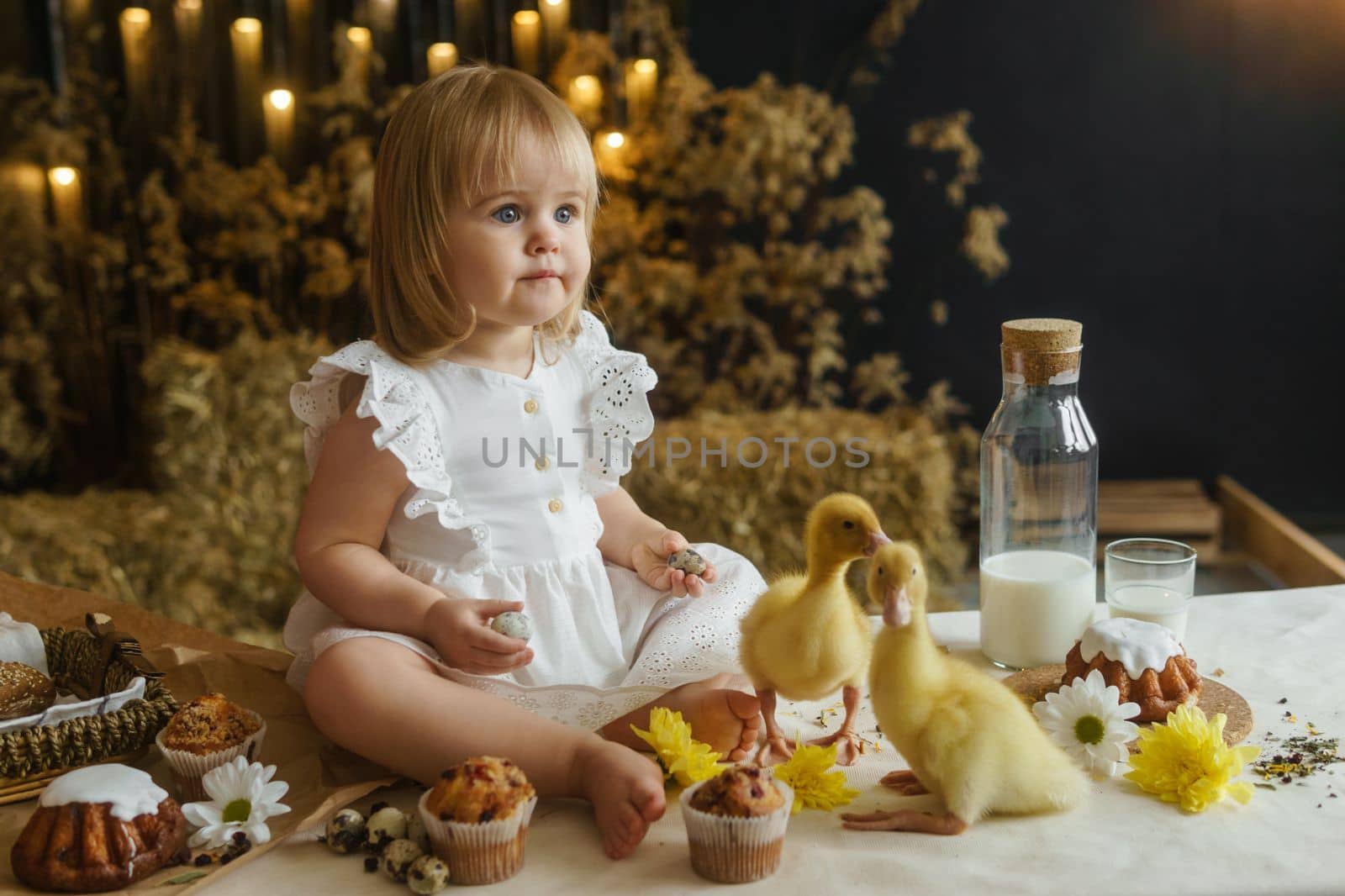 A little girl is sitting on the Easter table and playing with cute fluffy ducklings. The concept of celebrating happy Easter