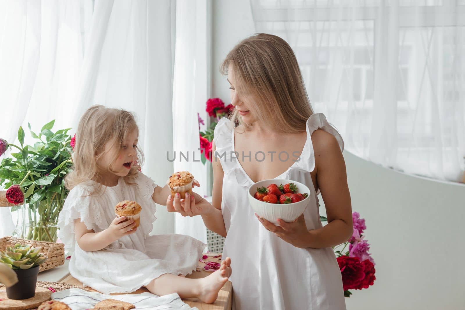 A little blonde girl with her mom on a kitchen countertop decorated with peonies. The concept of the relationship between mother and daughter. Spring atmosphere. by Annu1tochka