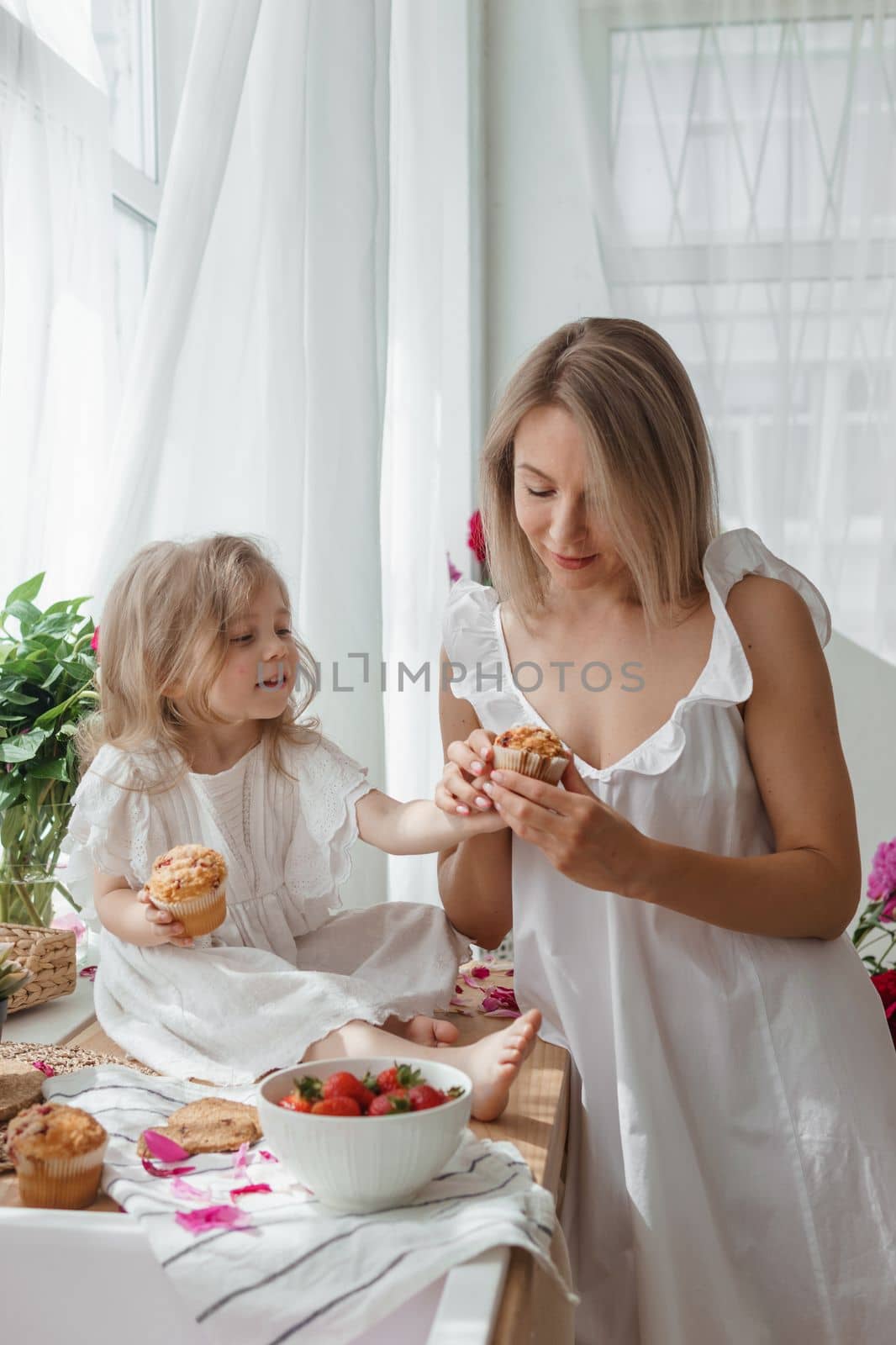 A little blonde girl with her mom on a kitchen countertop decorated with peonies. The concept of the relationship between mother and daughter. Spring atmosphere.