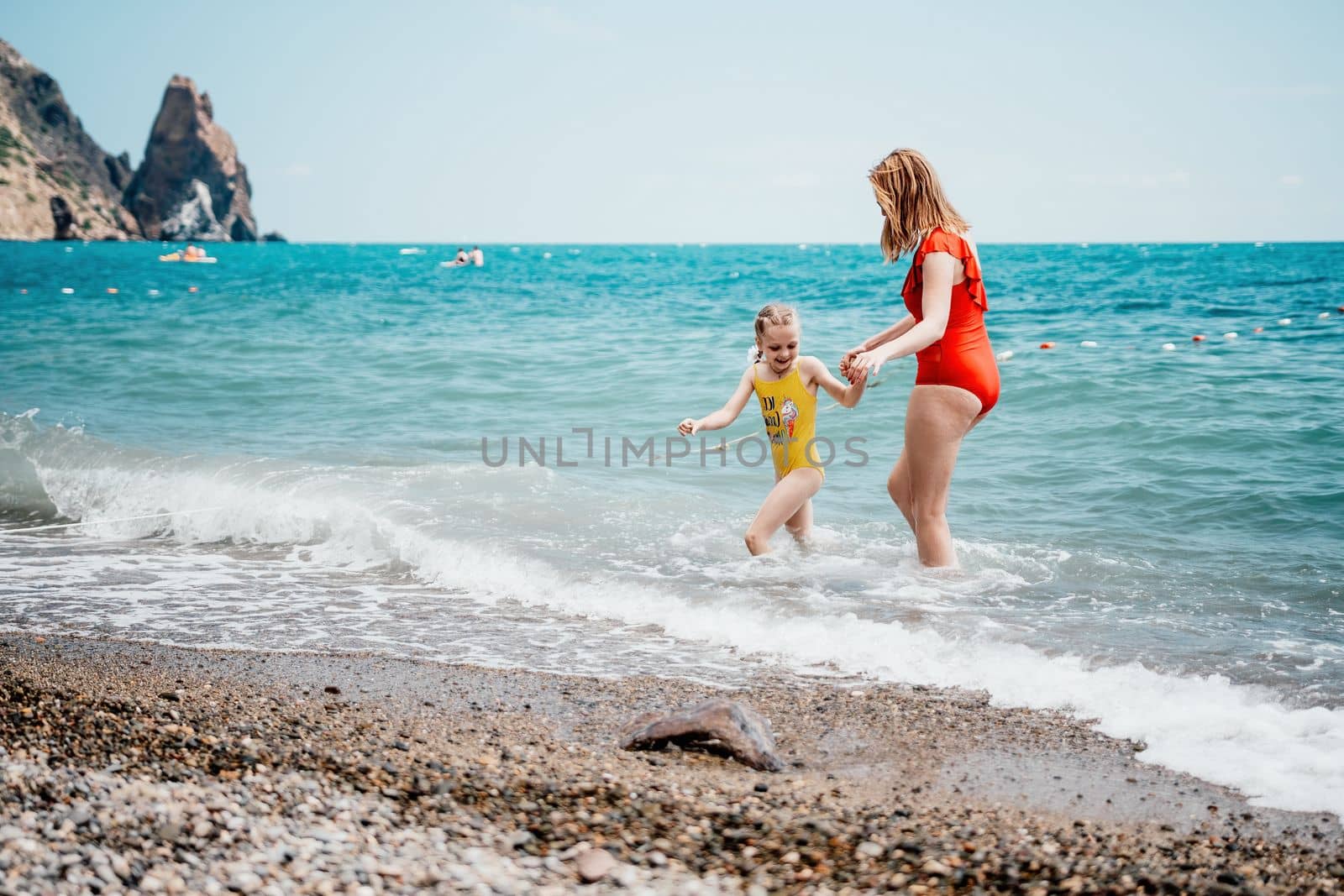 Happy loving family mother and daughter having fun together on the beach. Mum playing with her kid in holiday vacation next to the ocean - Family lifestyle and love concept.