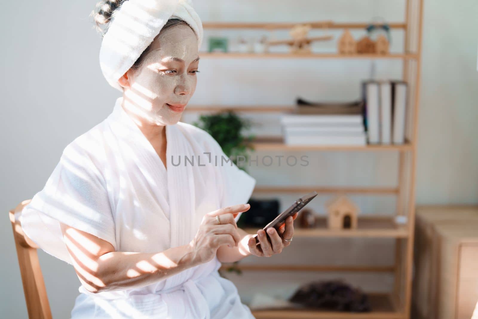 Portrait of elderly woman doing face spa treatment and using mobile phone. by Manastrong