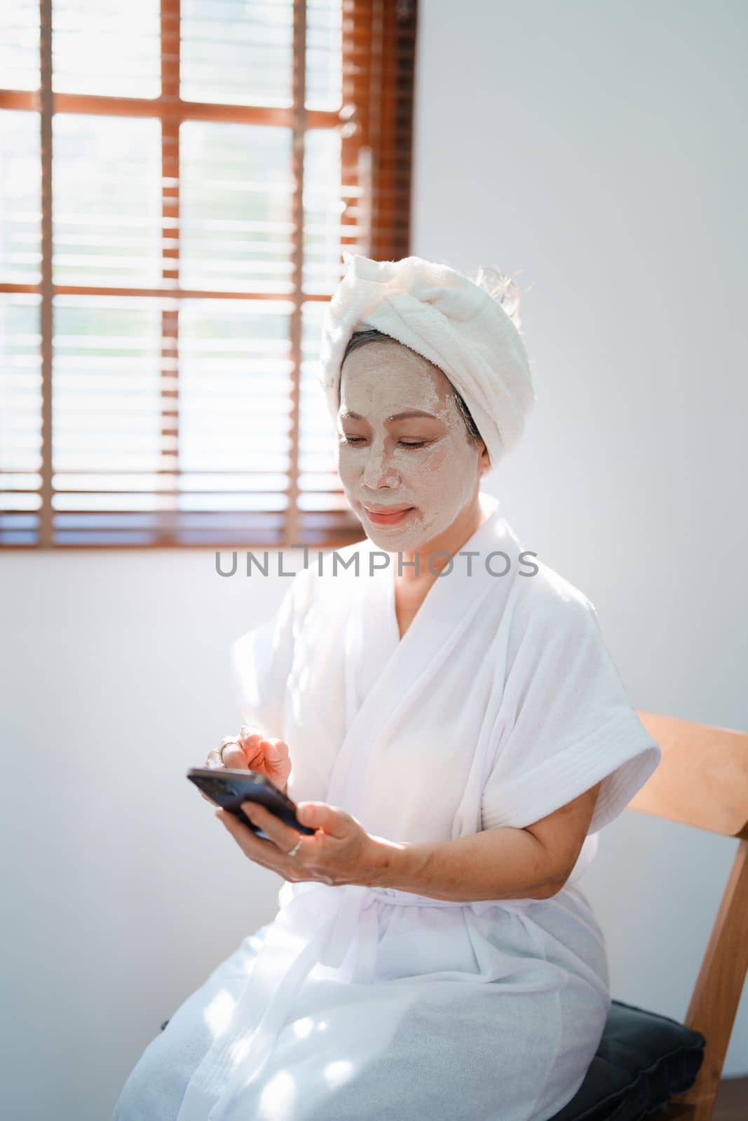 Portrait of elderly woman doing face spa treatment and using mobile phone. by Manastrong