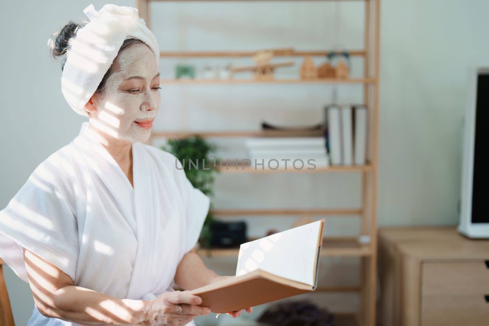 Portrait of elderly woman doing face spa treatment and using notebook. by Manastrong