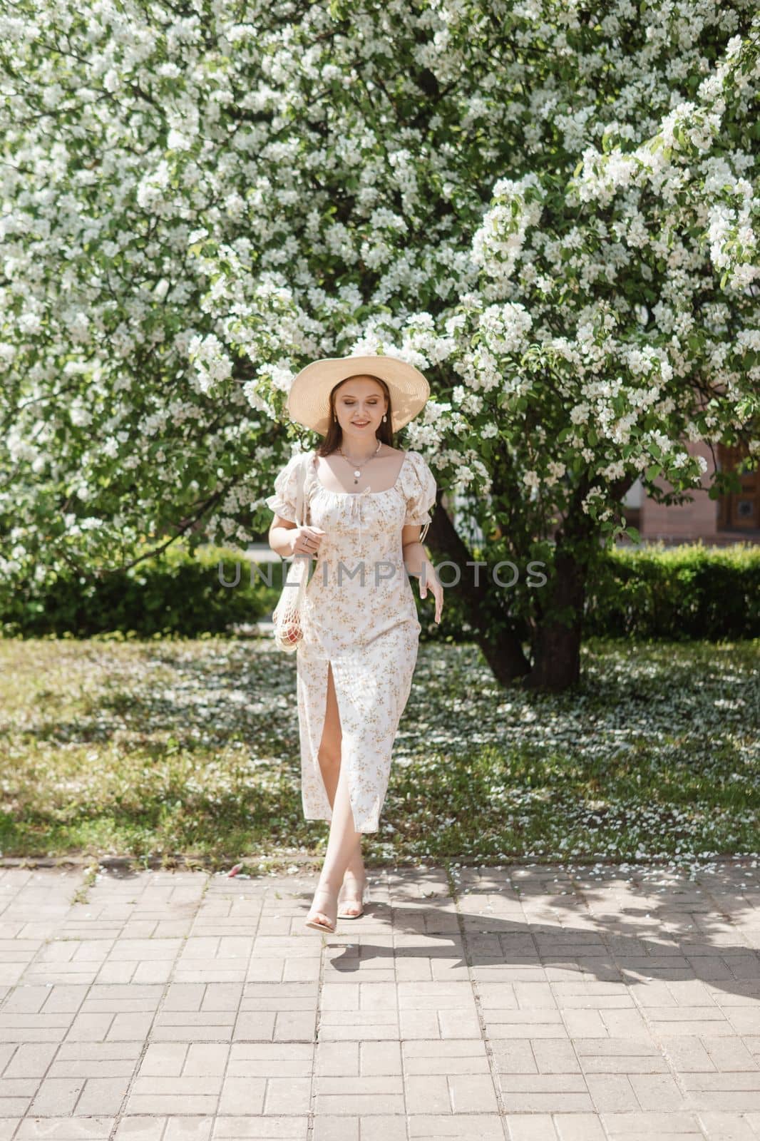 An attractive long-haired woman walks in the spring in the park of blooming apple trees. Spring portrait of a woman