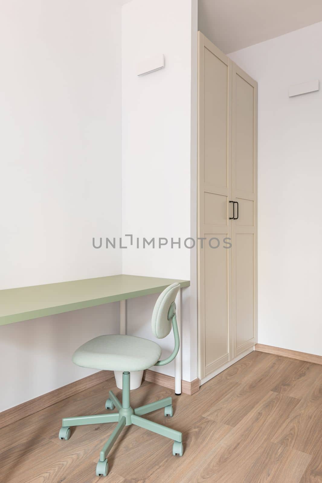 Part of the living room with white walls, built-in wardrobe, wood-effect parquet flooring. Against the wall is a work table with a mint-colored top and a mint-colored leather chair