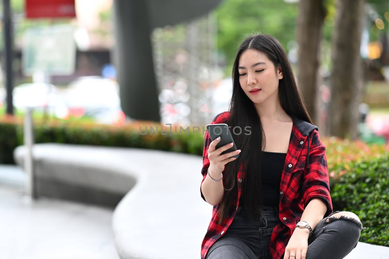 Young woman sitting outdoor in the city and using smart phone.