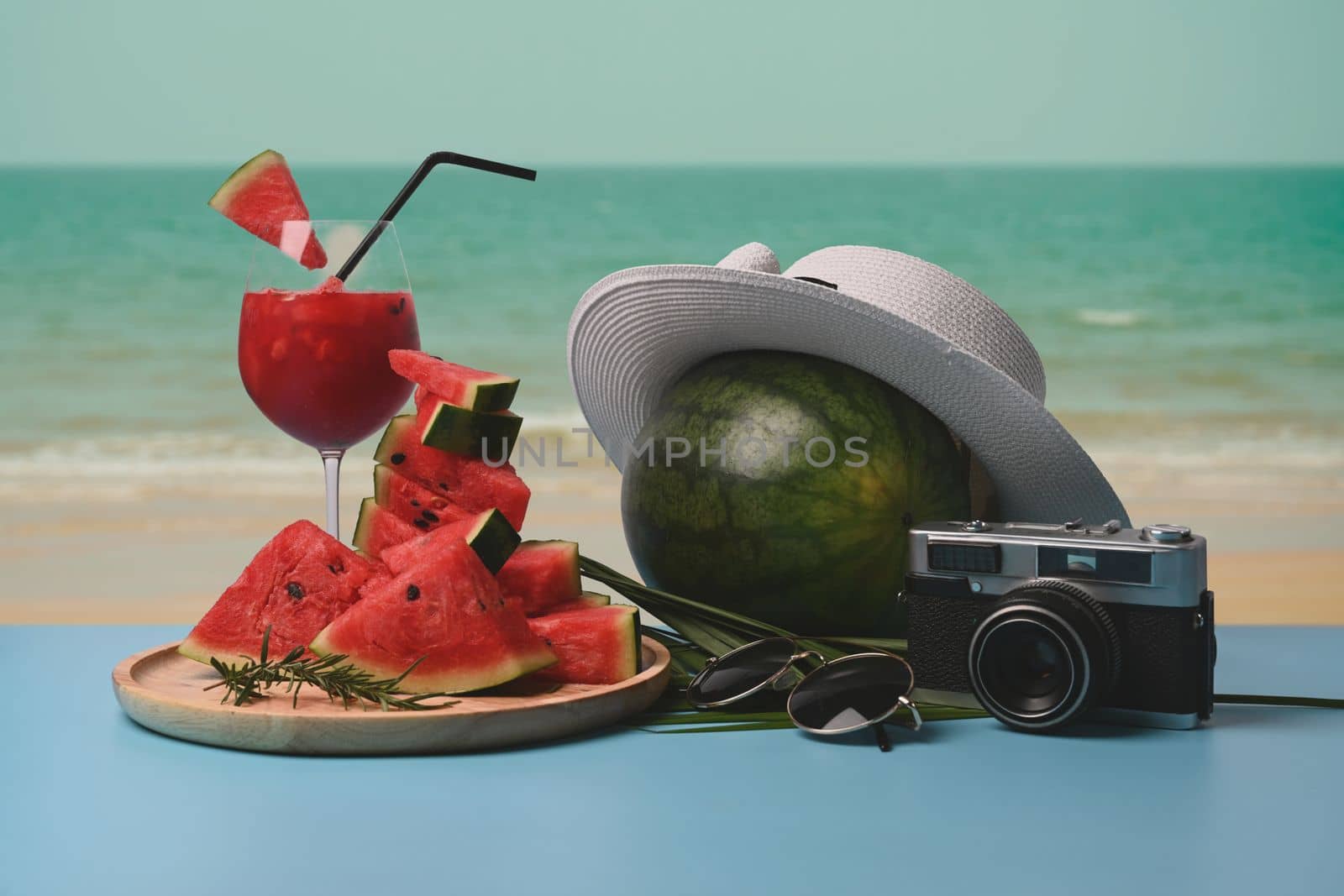 Sliced watermelon and watermelon smoothie on table with beautiful summer beach in background.