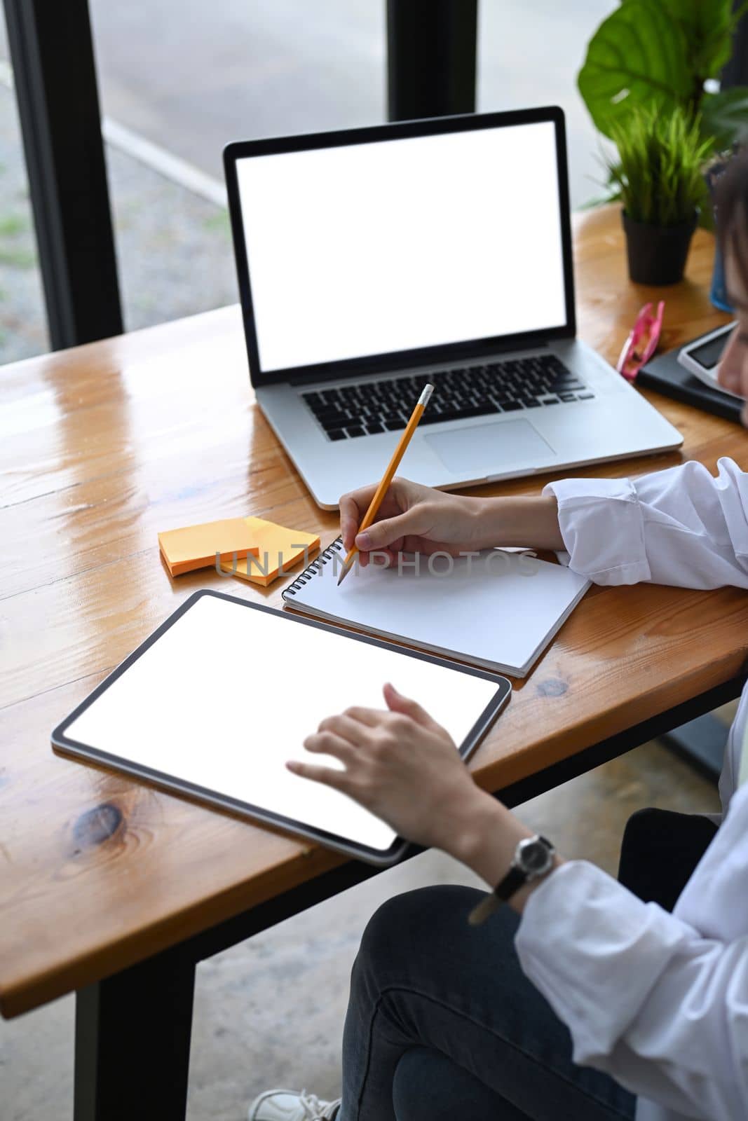 Female entrepreneur working with digital tablet and making note on notebook. by prathanchorruangsak